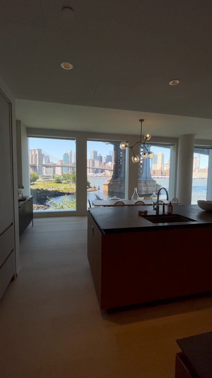 Modern apartment kitchen with large windows overlooking a city skyline and river bridge.