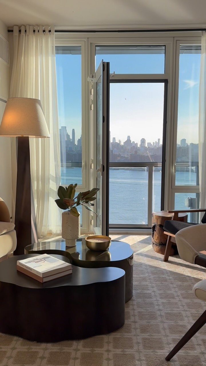 Modern apartment interior with a balcony overlooking a river and city skyline.