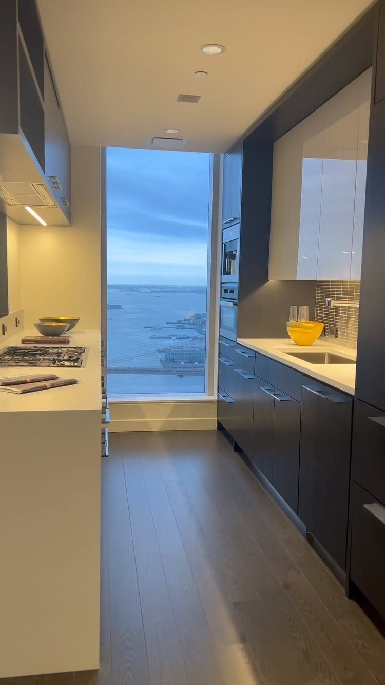 Modern kitchen with dark cabinets and a large window overlooking a waterfront city.