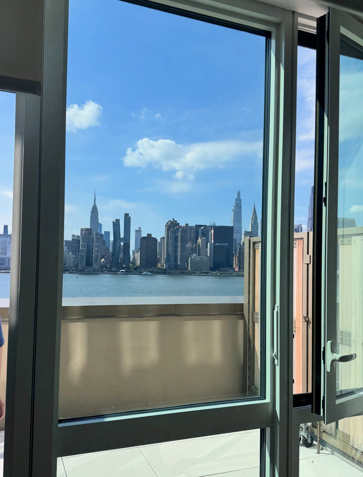 Manhattan skyline and river viewed through an open apartment window under blue sky