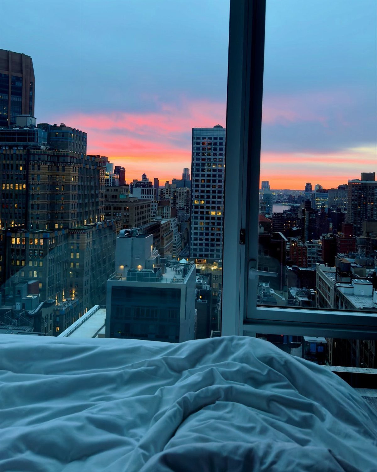City skyline at sunset viewed from a high-rise apartment bedroom window.