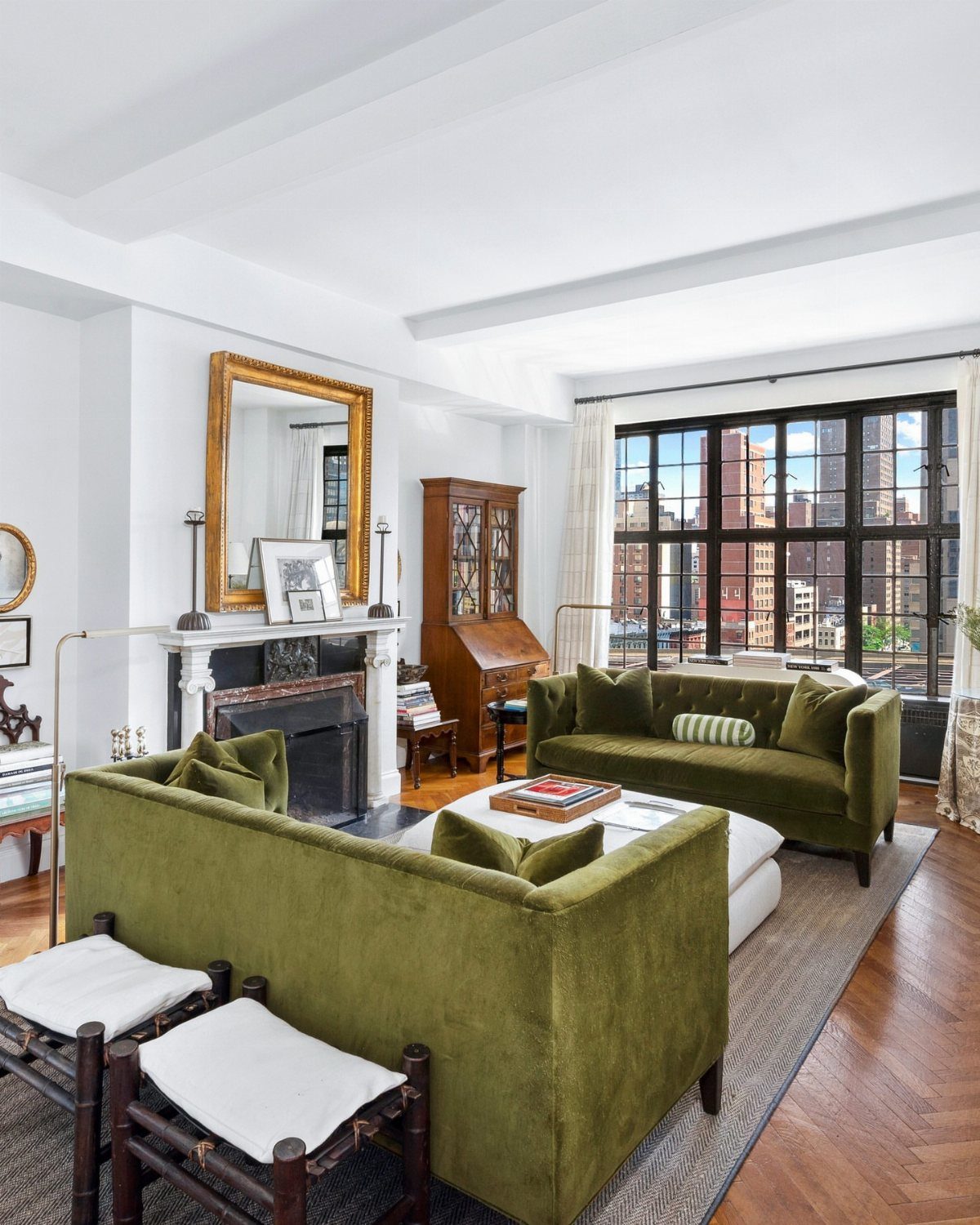 Living room with olive green sofas and a window view of NYC buildings.