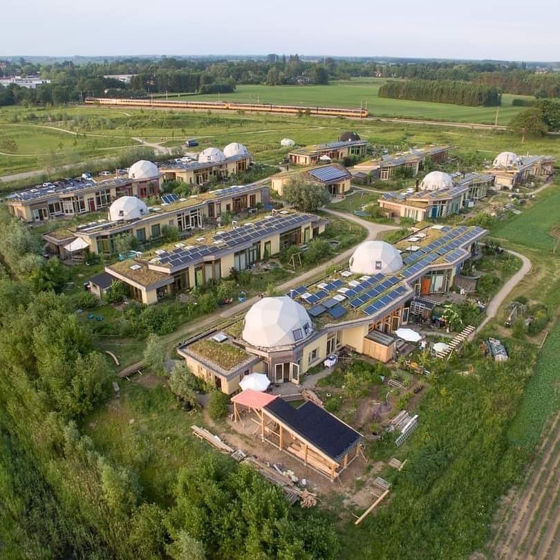 Sustainable community buildings with white domes, solar panels, and green roofs in countryside