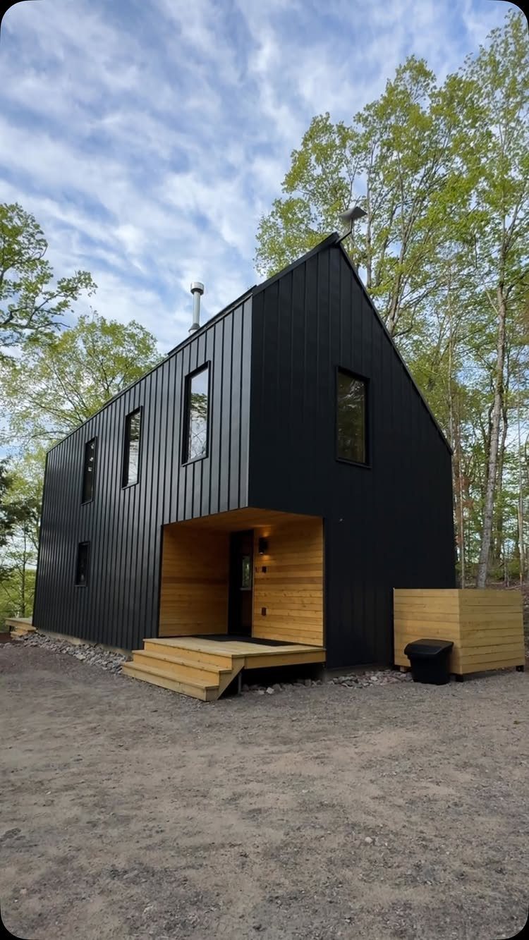 Modern black metal gabled house with wooden porch in a wooded setting