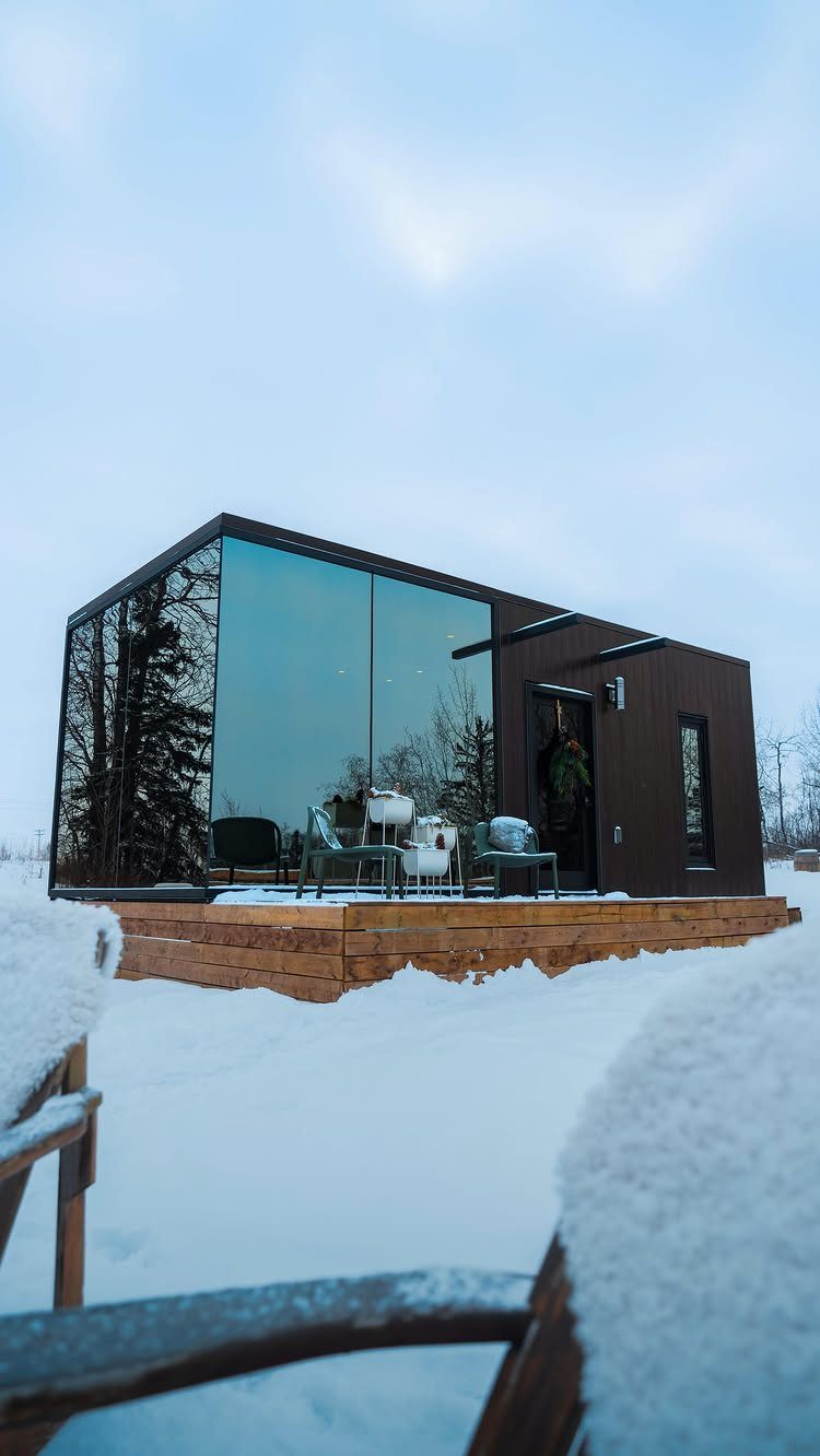 Modern small dark-brown house with large glass windows in a snowy winter landscape