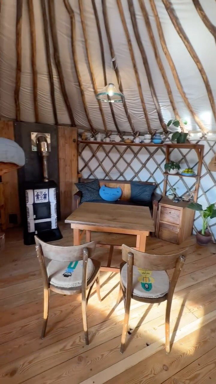 Interior of a yurt home featuring wooden furniture and a wood-burning stove.