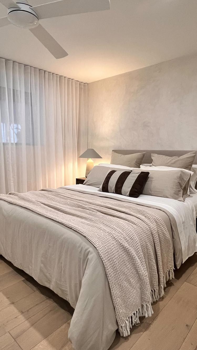 Bed with beige linens next to white curtains hanging from the ceiling.
