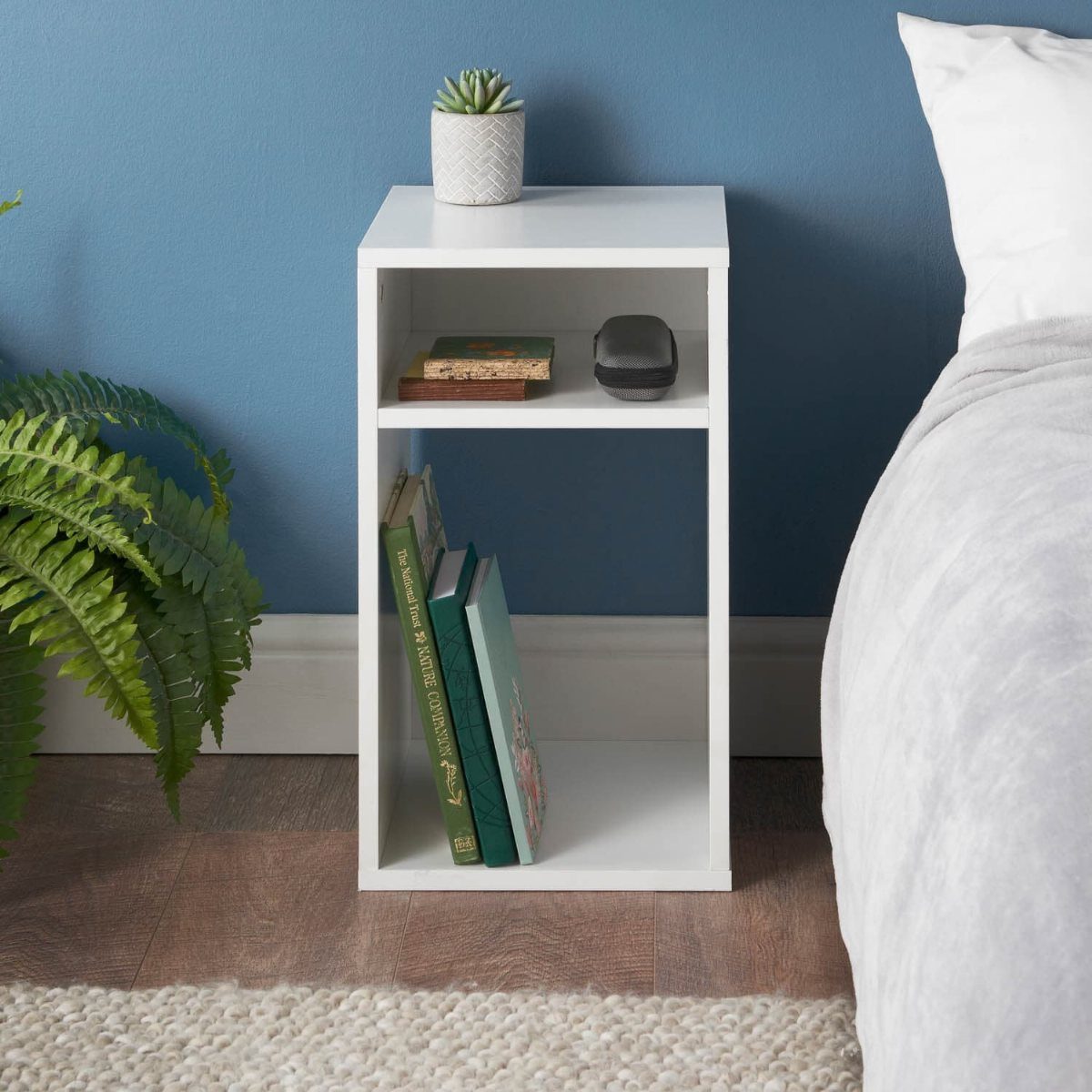 White open shelving bedside table with books and a small potted succulent plant.