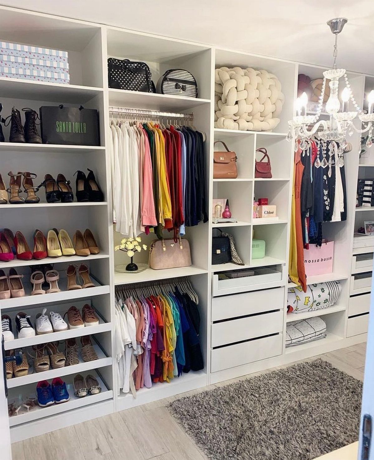 White built-in shelving system organizing shoes, handbags, and colorful hanging clothes in a closet.