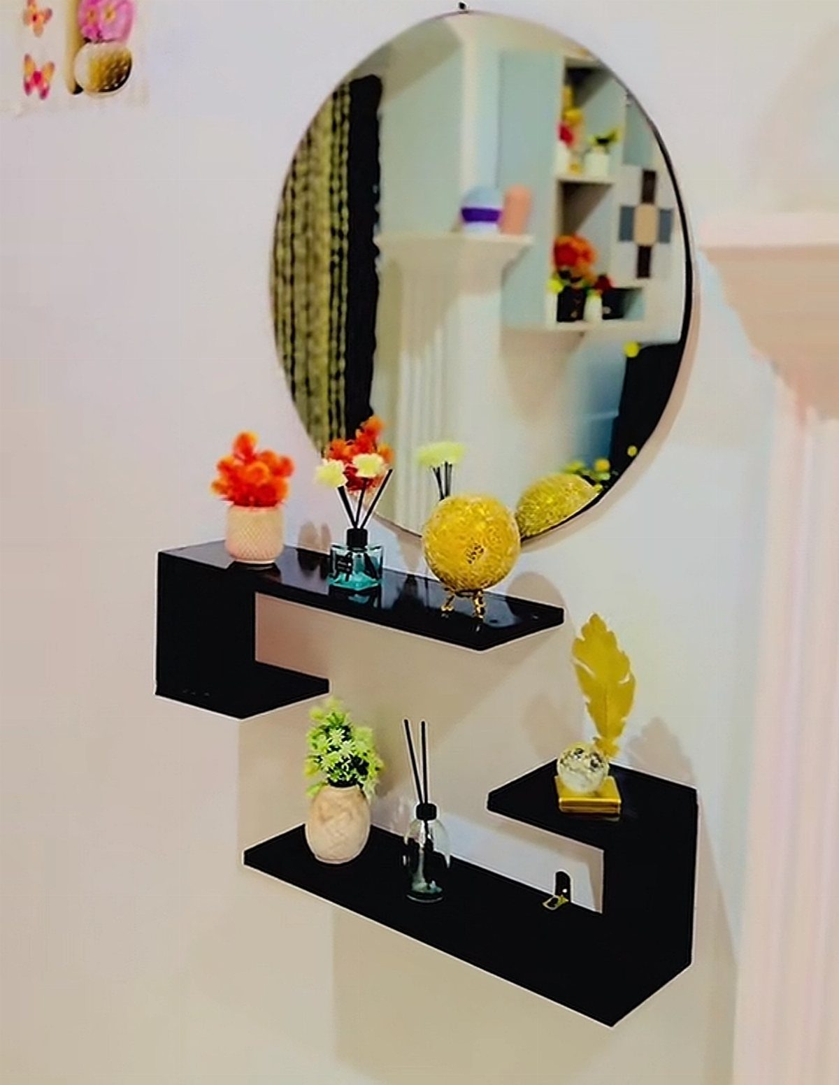 Round mirror and black geometric floating shelves with colorful flowers on white wall