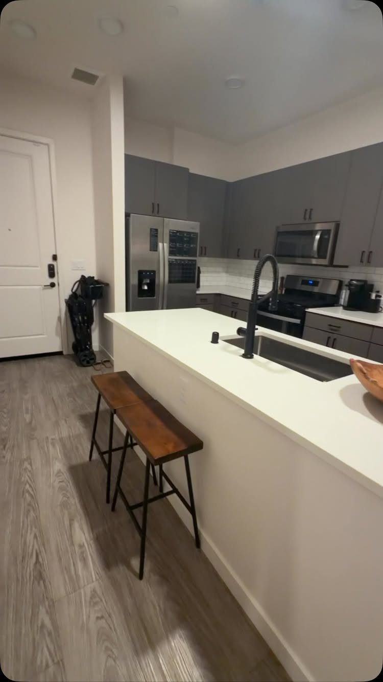 Modern kitchen with grey cabinets, white island, and wooden bar stools.