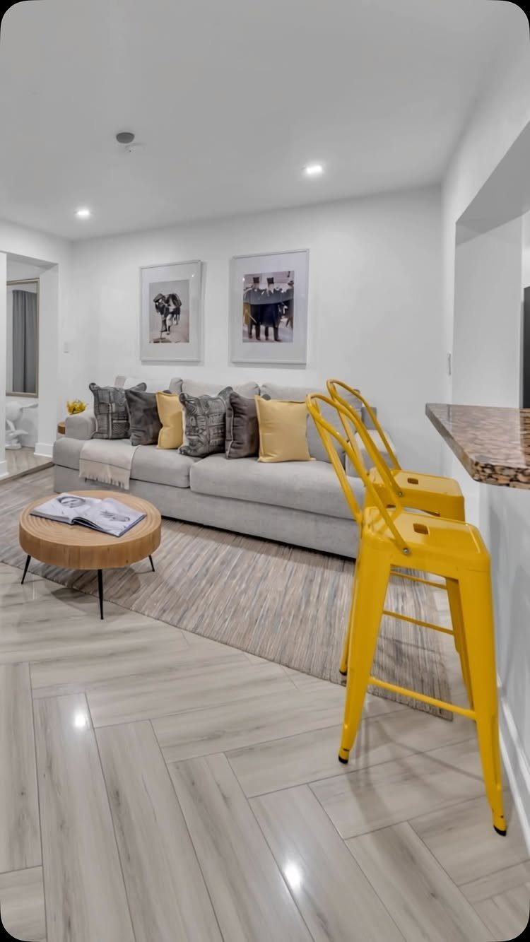 Grey sofa and yellow barstools in a studio apartment with framed wall art.