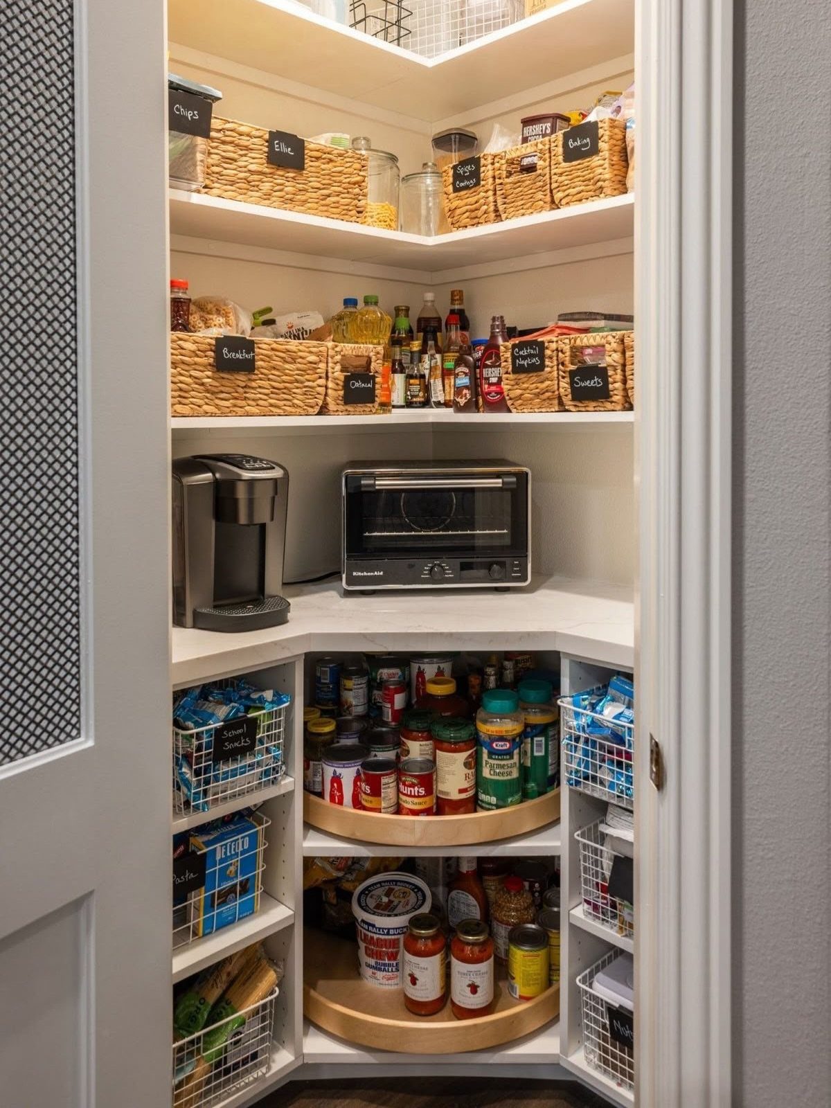 White built-in pantry closet with woven baskets and top-shelf storage for kitchen supplies.
