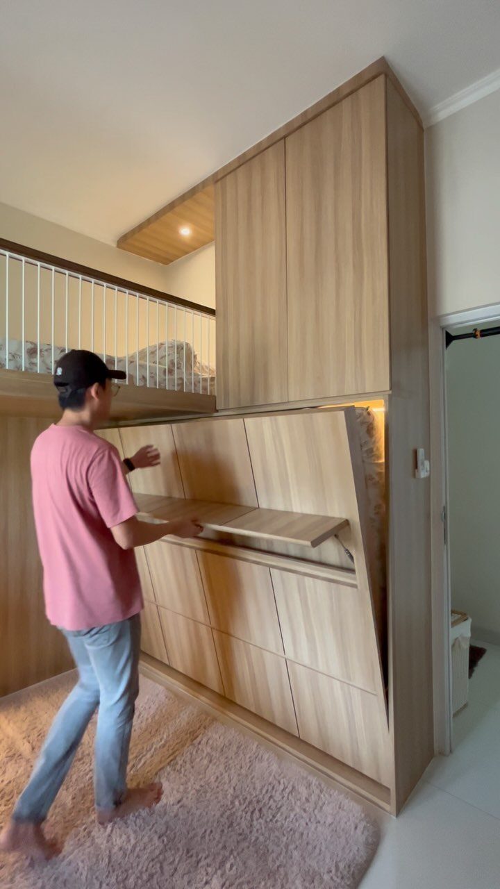 Man using a fold-down wooden desk attached to a light wood wall unit.