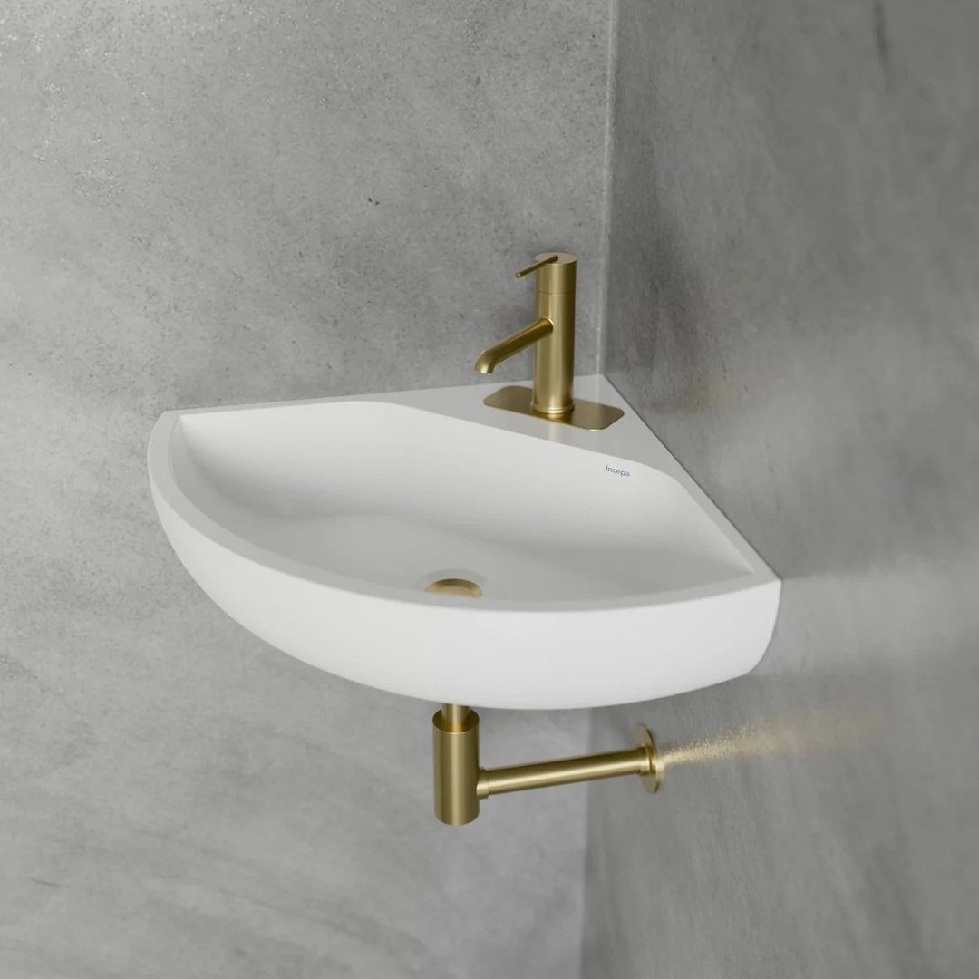 White curved wall-mounted sink with gold faucet against a grey concrete wall.