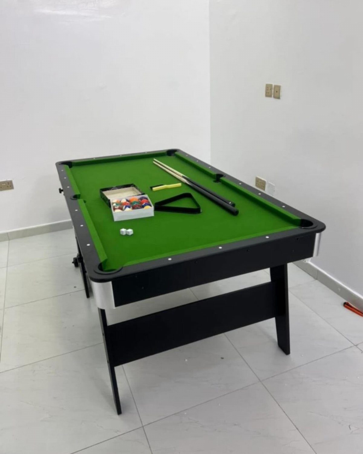 Small black pool table with green felt and accessories in a white room