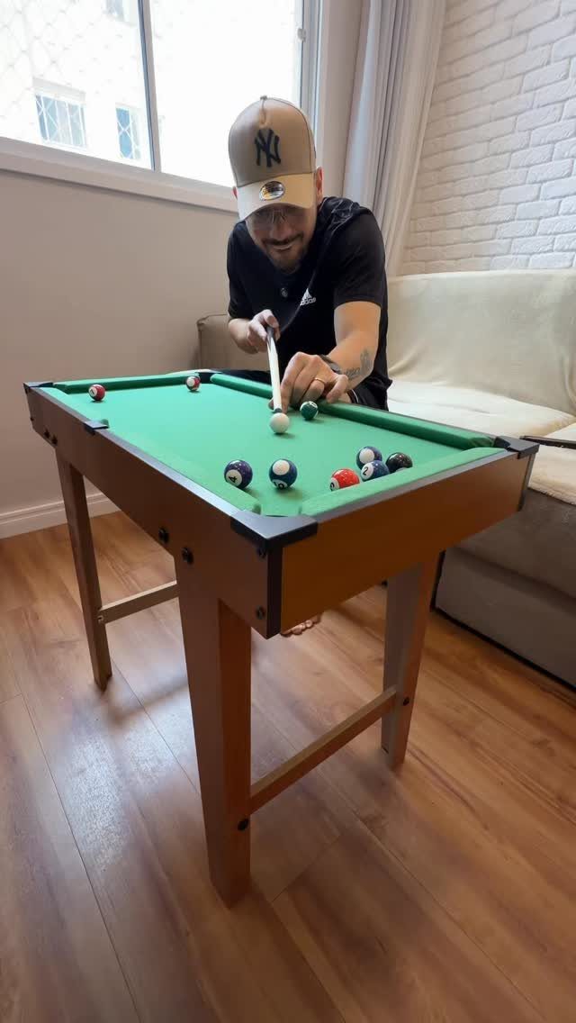 Man playing on a compact wooden pool table in a small living room