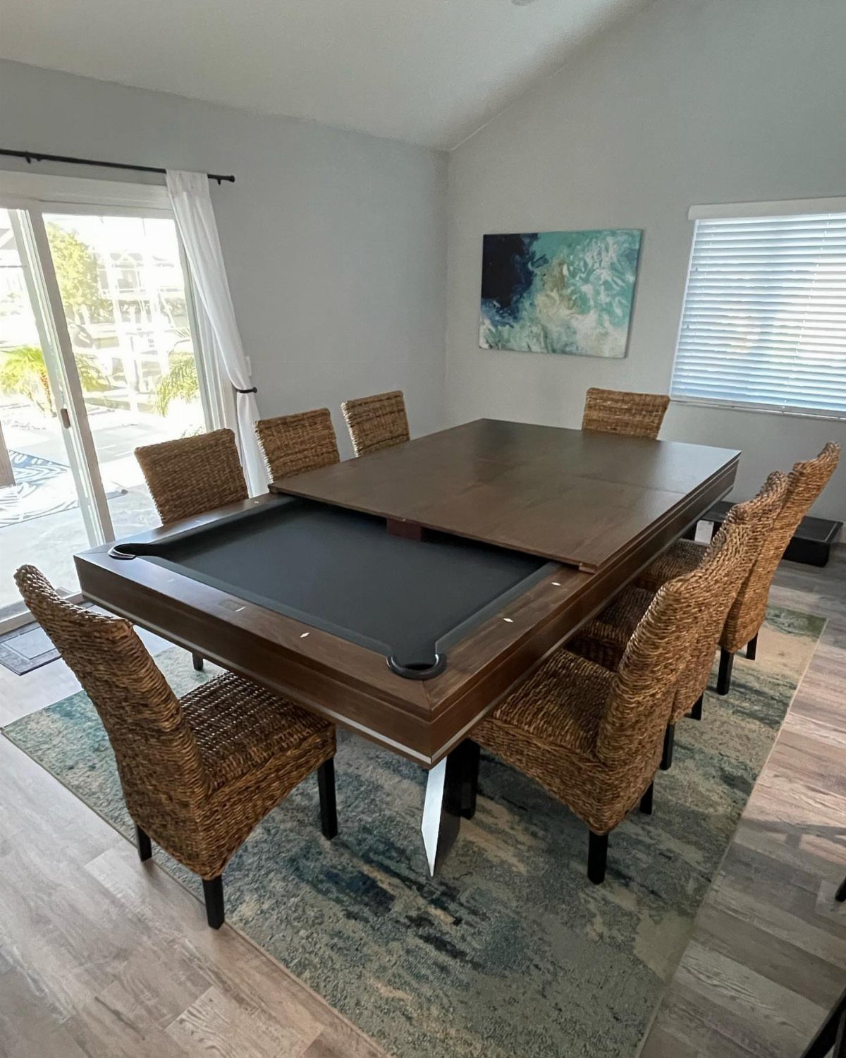 Convertible pool table with a dining surface and woven wicker chairs in a room.