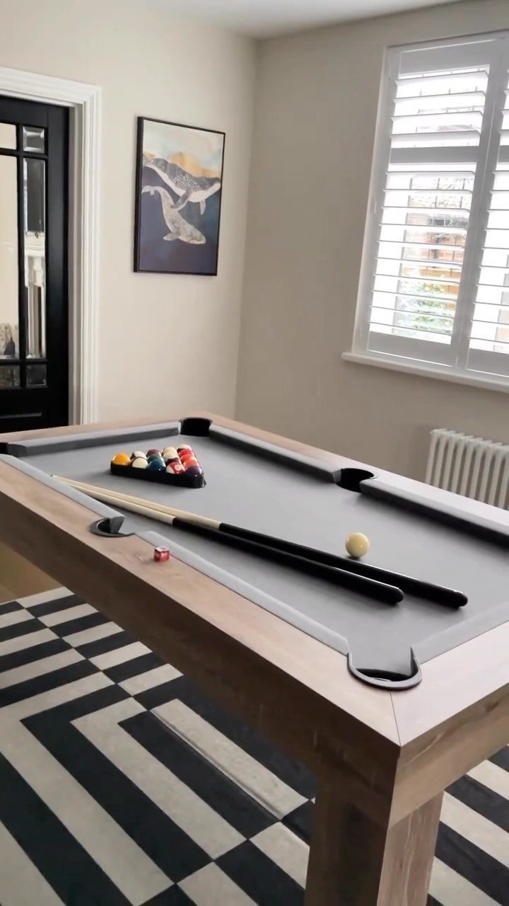 Grey felt pool table in a small room with geometric rug and shutters