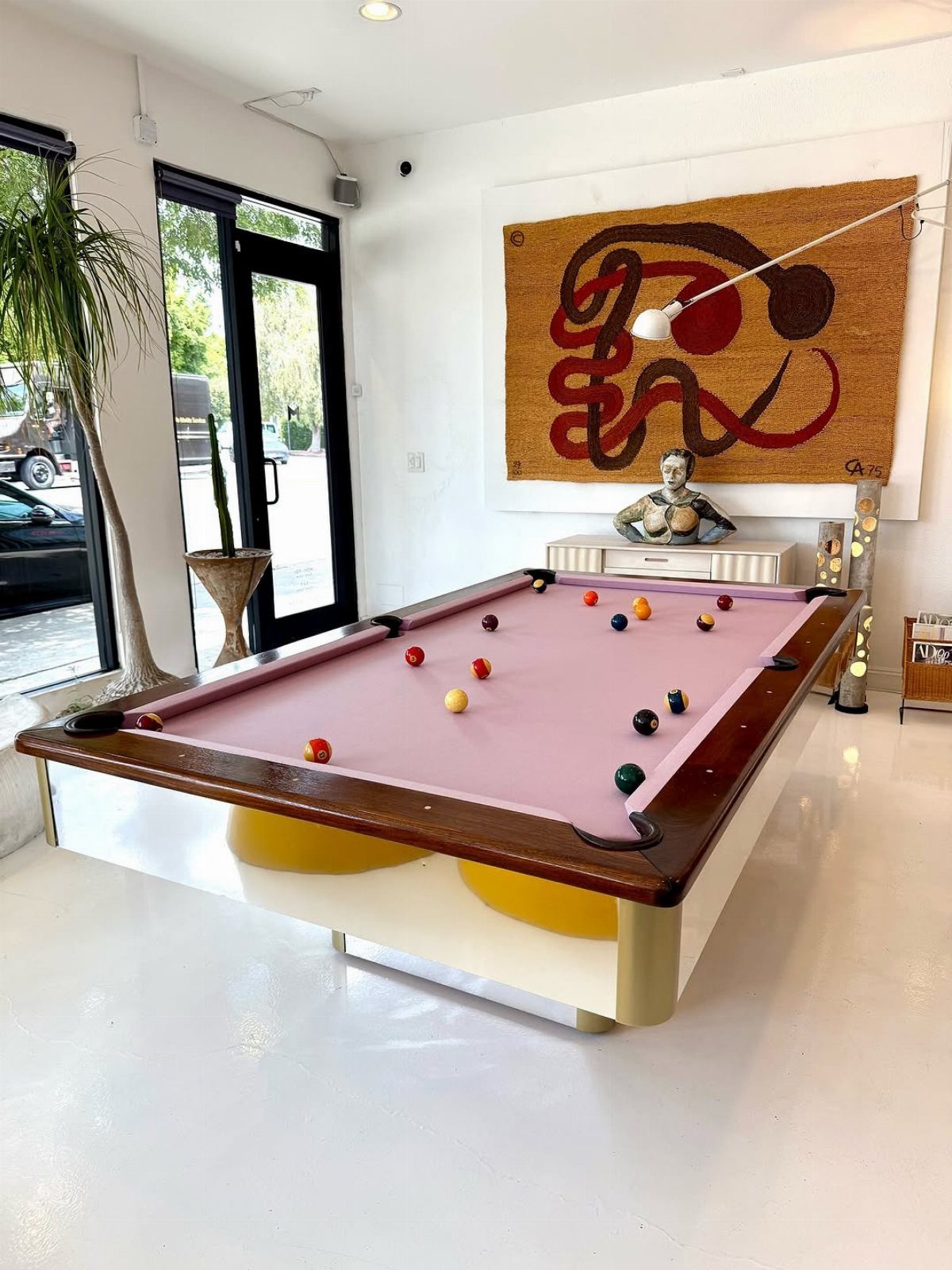 Pink felt pool table in a bright white room with abstract wall art.
