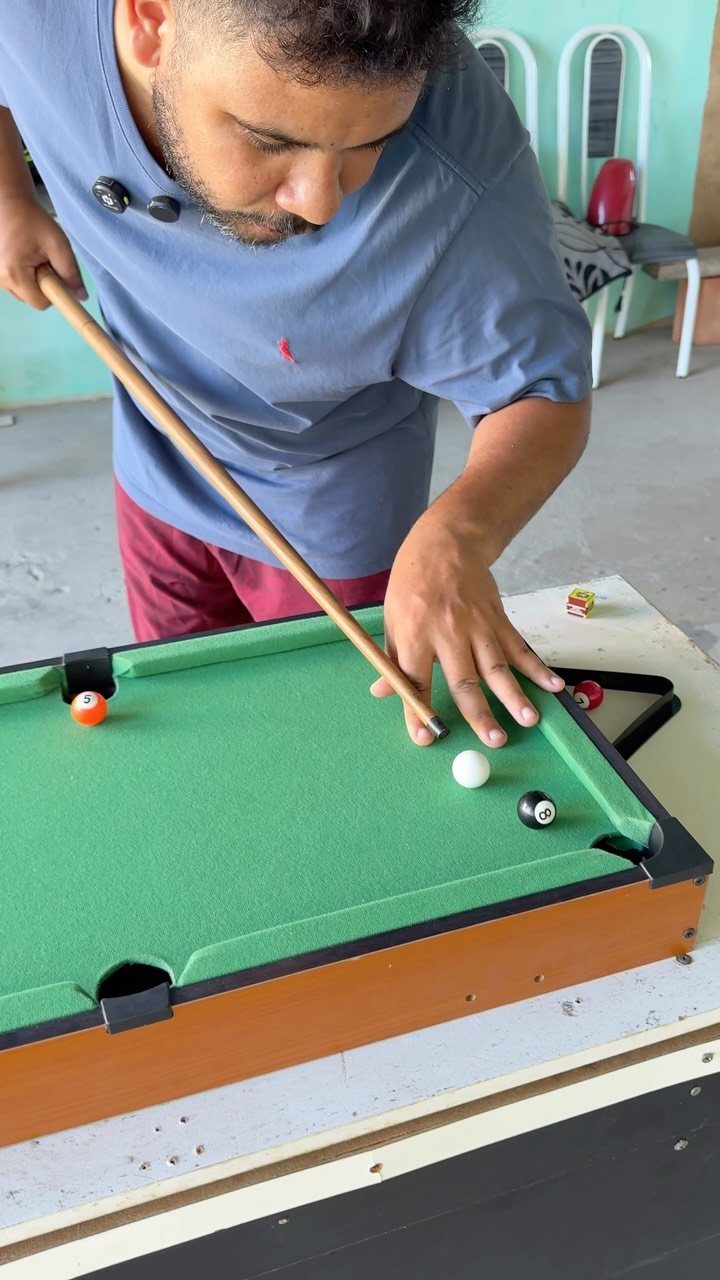 Man playing on a small portable pool table with green felt and wooden base.