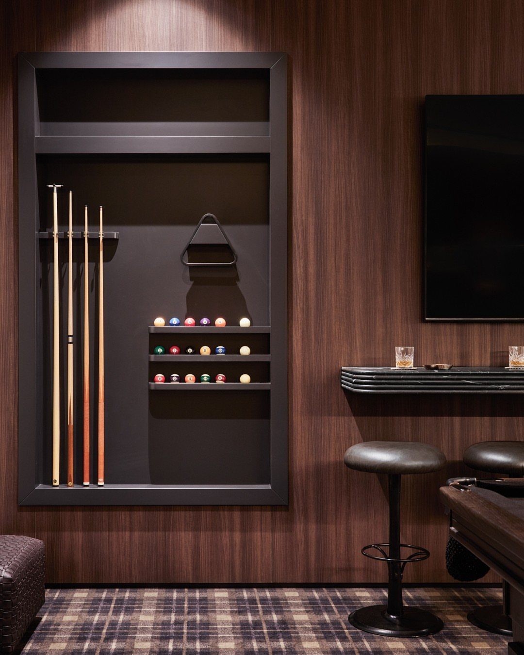 Built-in black wall rack holding pool cues and billiard balls in a modern room.