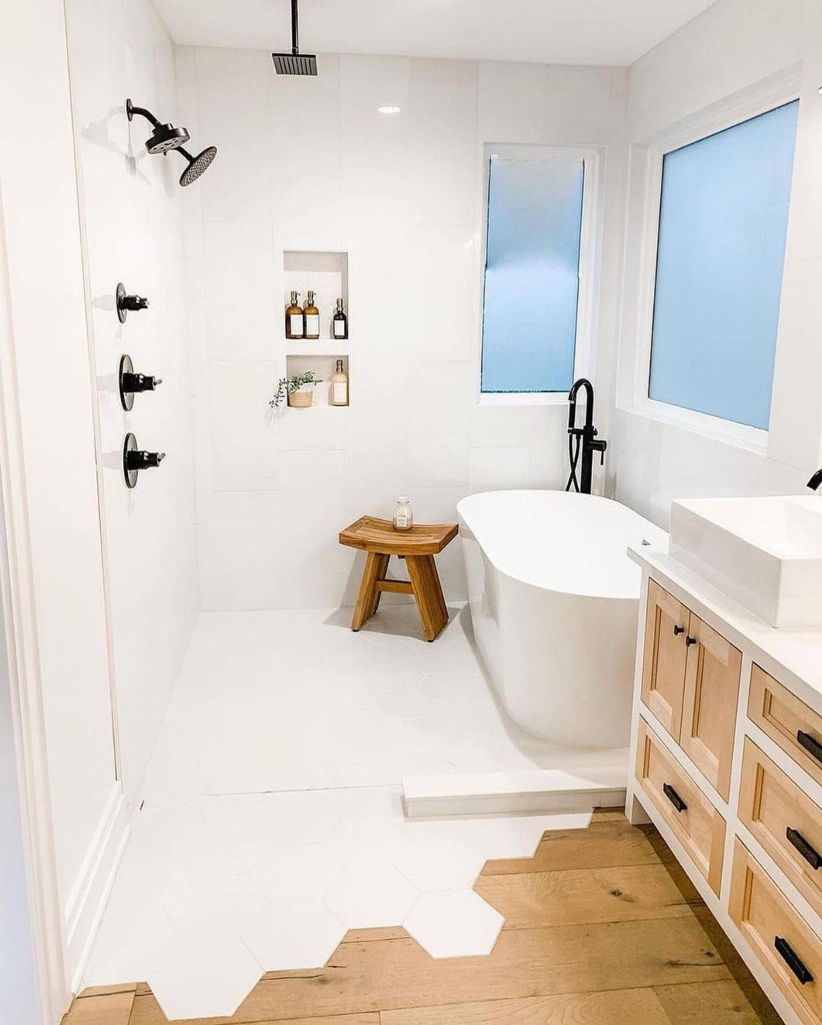 Modern white bathroom with freestanding tub, black shower fixtures, and hexagonal floor tiles.