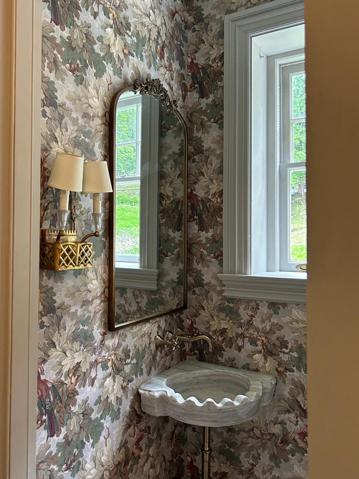 White marble corner sink with gold faucet against floral wallpapered bathroom walls.