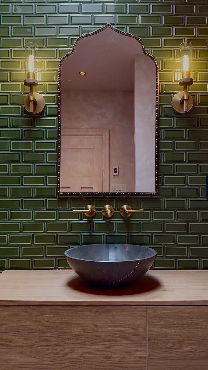 Dark grey vessel sink on wood counter against a green tiled wall.