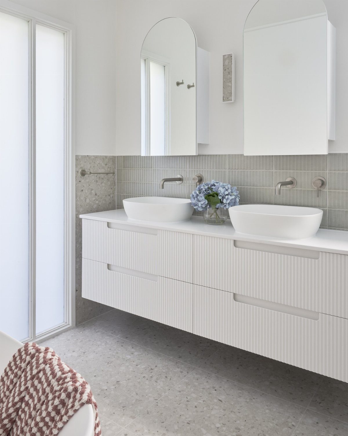 Modern white bathroom with floating vanity, double vessel sinks, and arched mirrors.