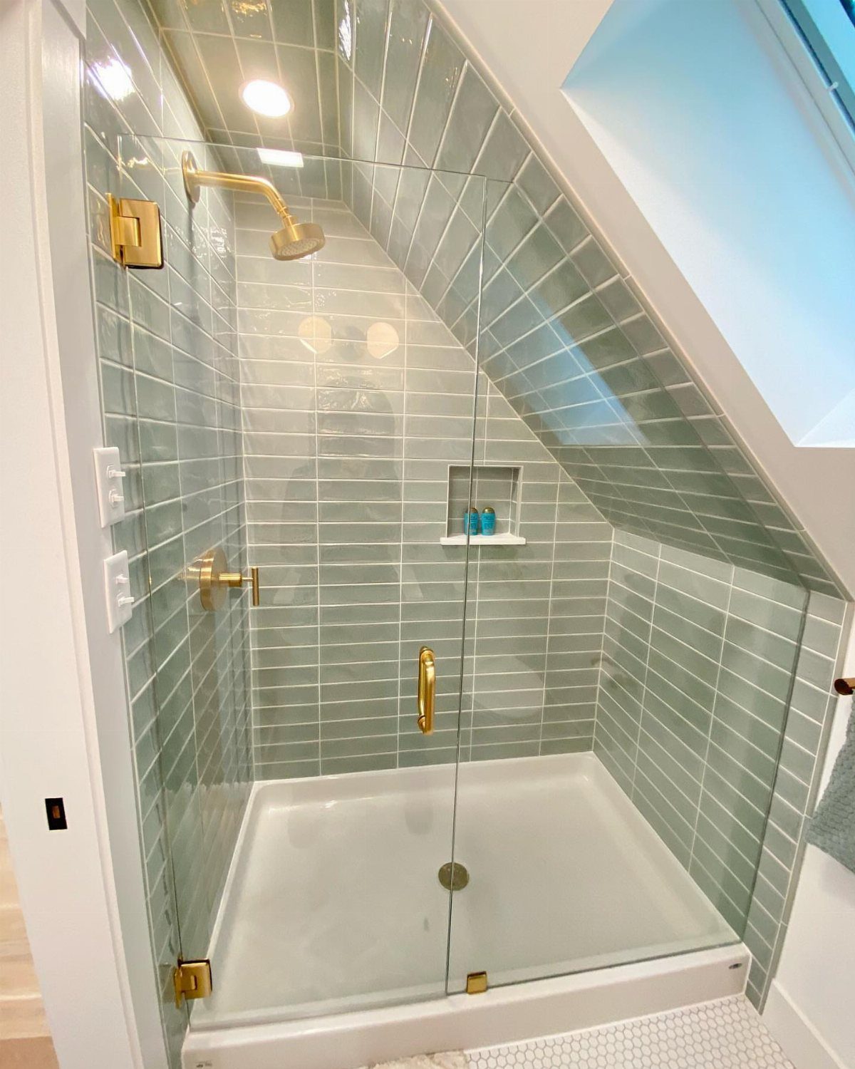 Modern walk-in shower with light blue tiles and a bright ceiling skylight.