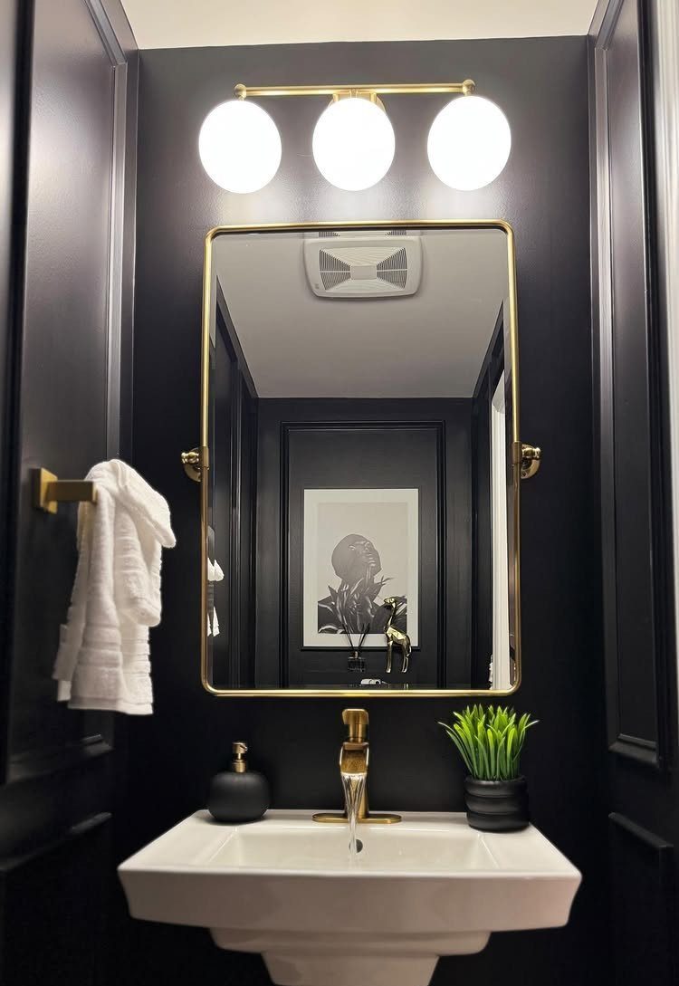 White pedestal sink and gold-framed mirror against black walls in a small bathroom
