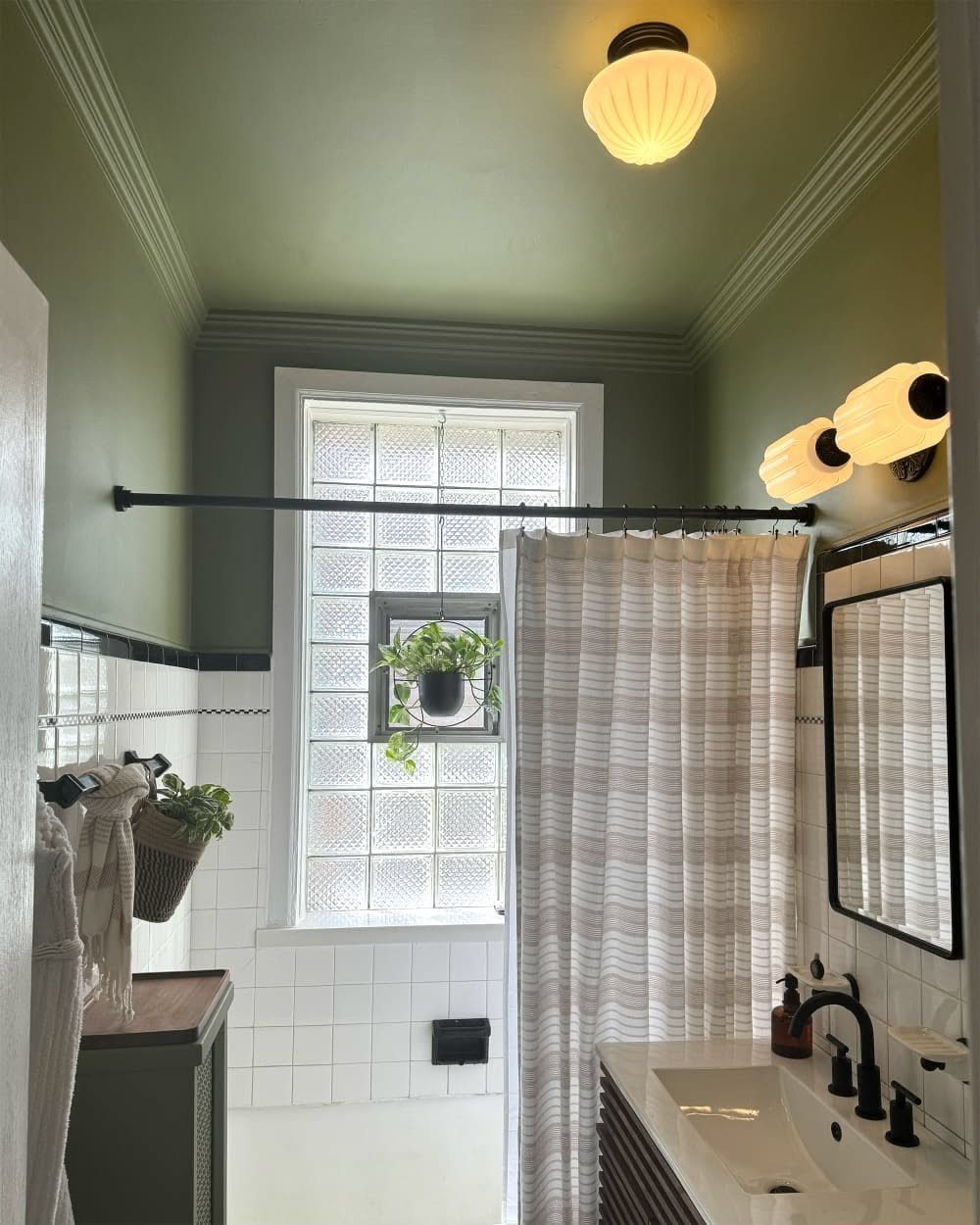 Sage green ceiling and walls in a bathroom with white tiles and lighting.