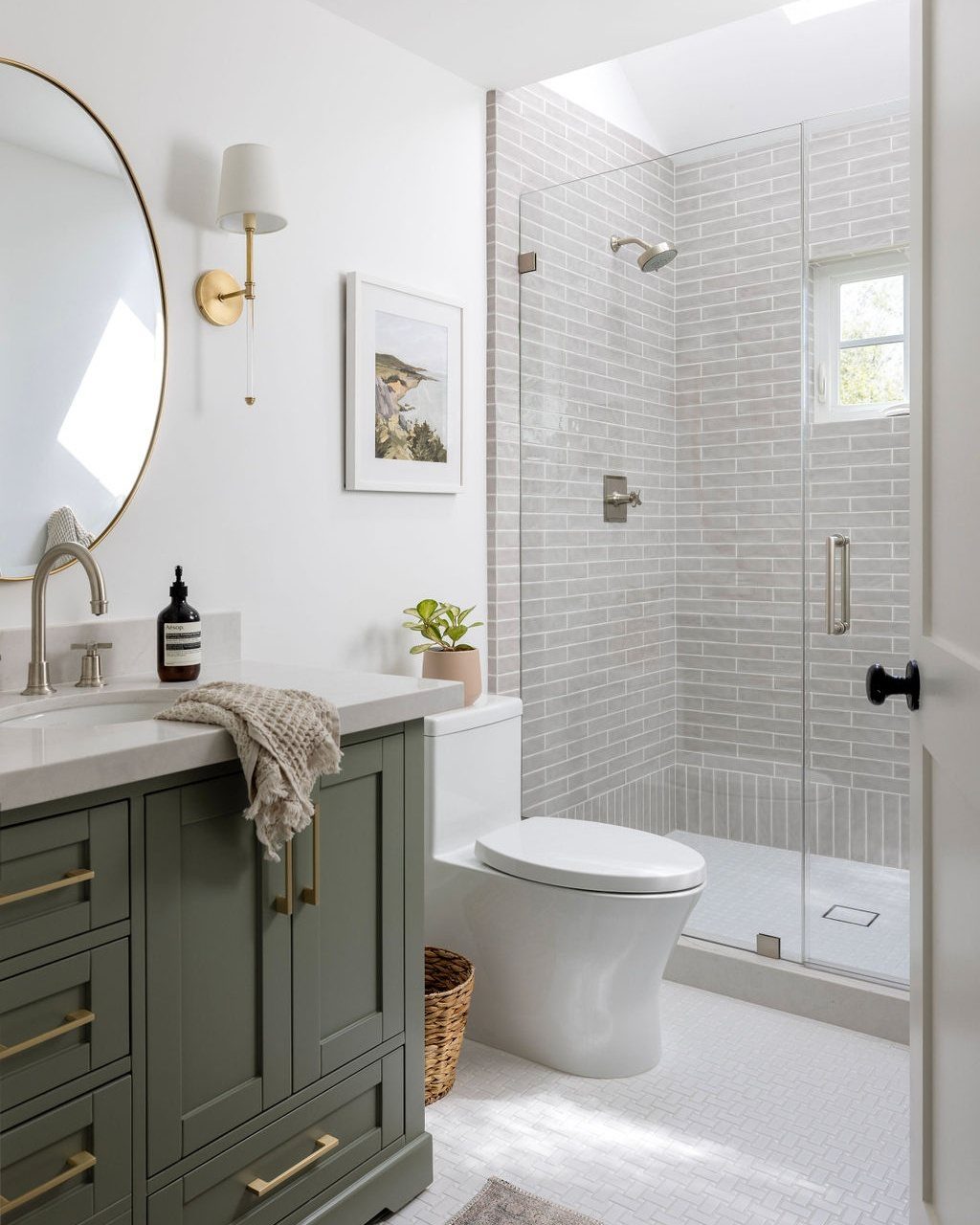 Sage green bathroom vanity with gold handles next to a white toilet and shower.