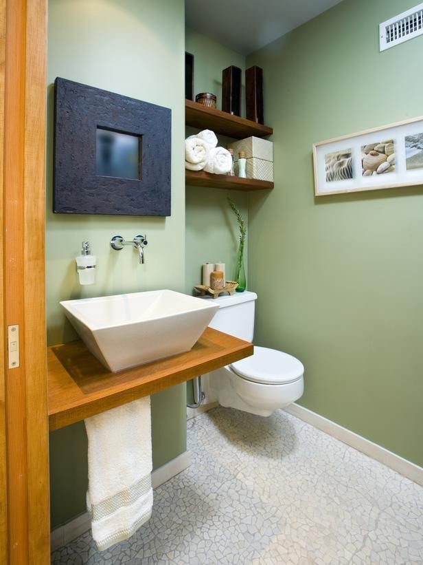 Sage green bathroom walls with a white vessel sink and wooden floating shelves.