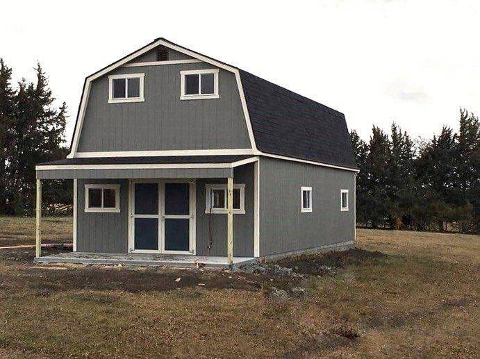 Grey gambrel-roofed shed with a loft level and a small front porch.