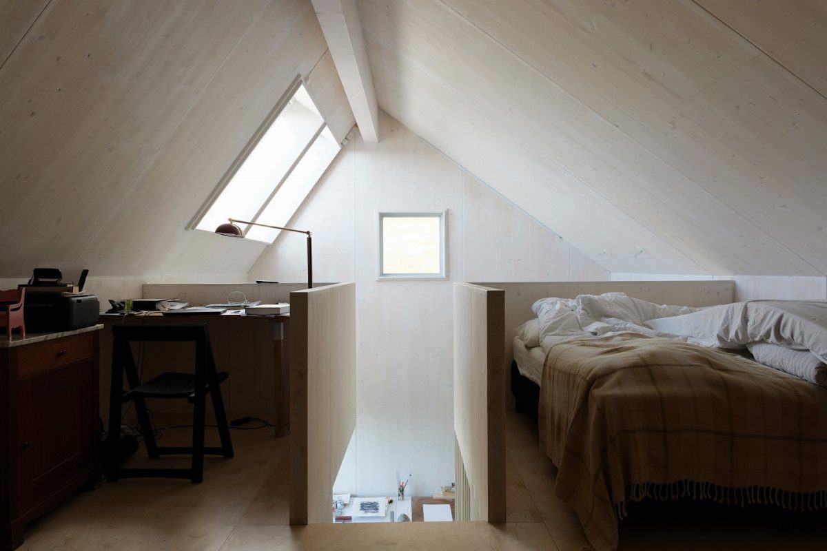 Loft sleeping area with a bed, desk, and white slanted wooden ceilings.
