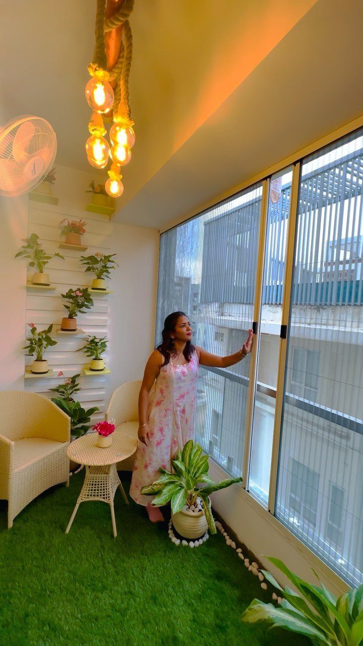 Woman on a small balcony with artificial grass, wicker furniture, and wall planters.