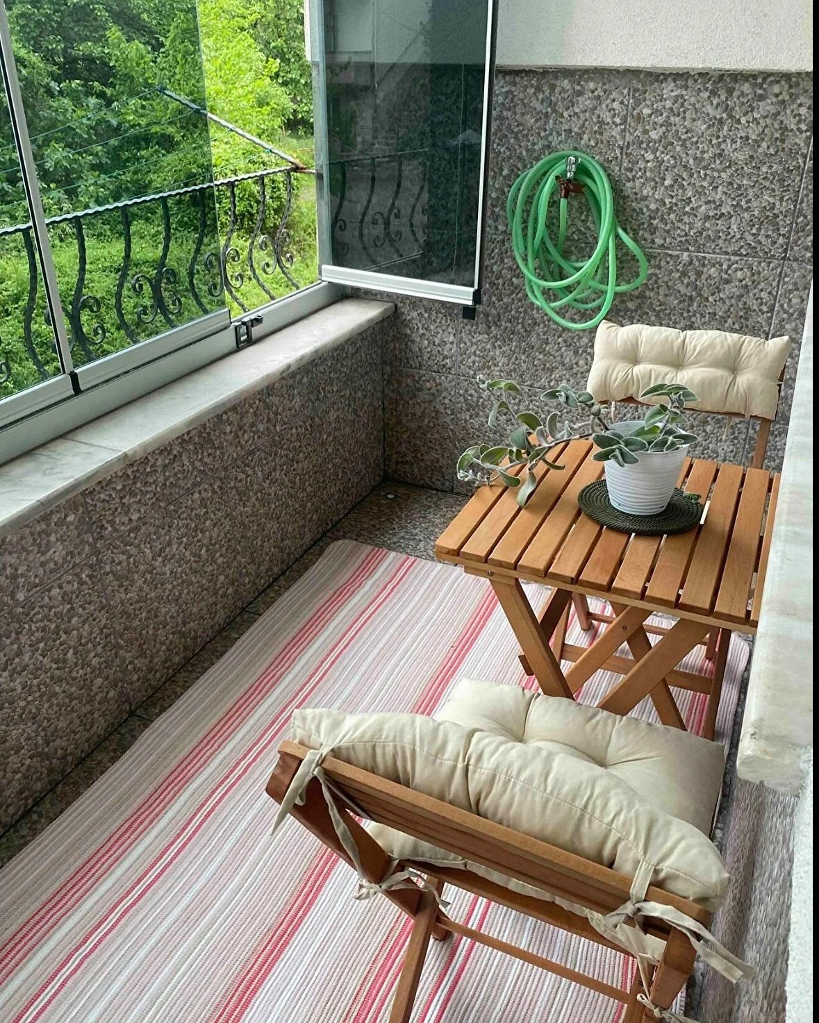 Wooden foldable table and chairs with cushions on a striped balcony rug.