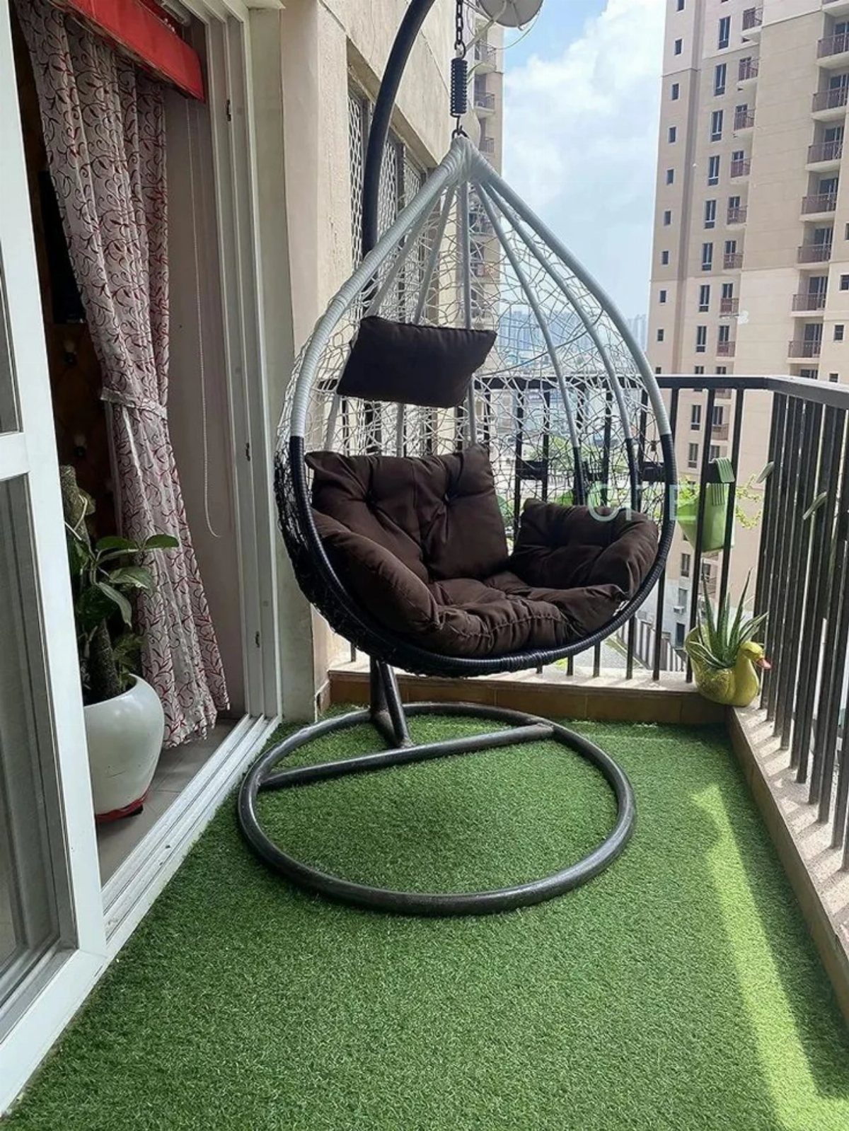 Hanging teardrop swing chair with brown cushions on a balcony with artificial grass.