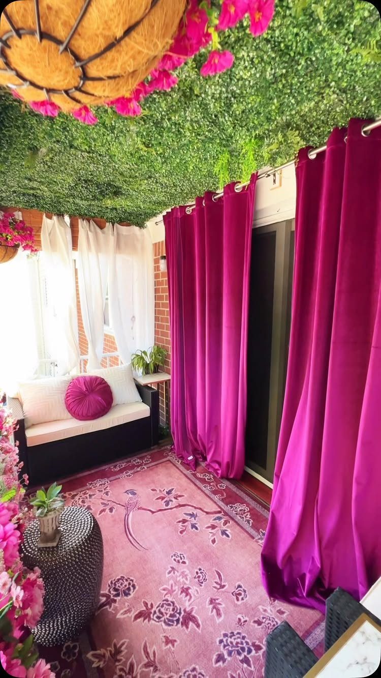 Magenta outdoor curtains and a pink floral rug on a decorated small balcony.