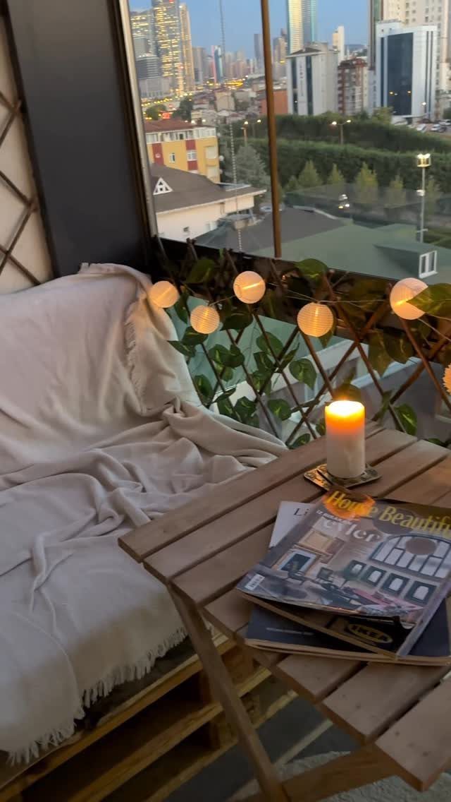 Wooden pallet lounge with white cushions and a small table on a city balcony.