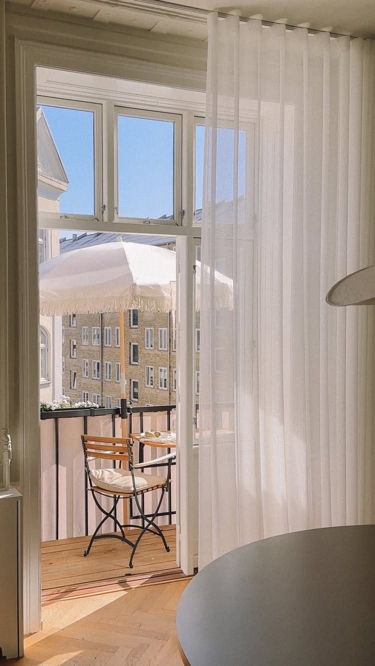 White fringed shade umbrella over a bistro set on a small city balcony.