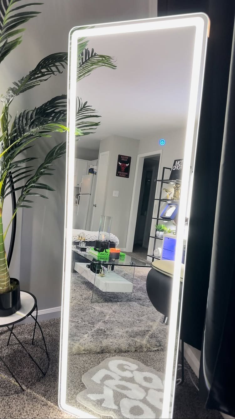 Full-length LED mirror reflecting a modern living room with a glass coffee table.