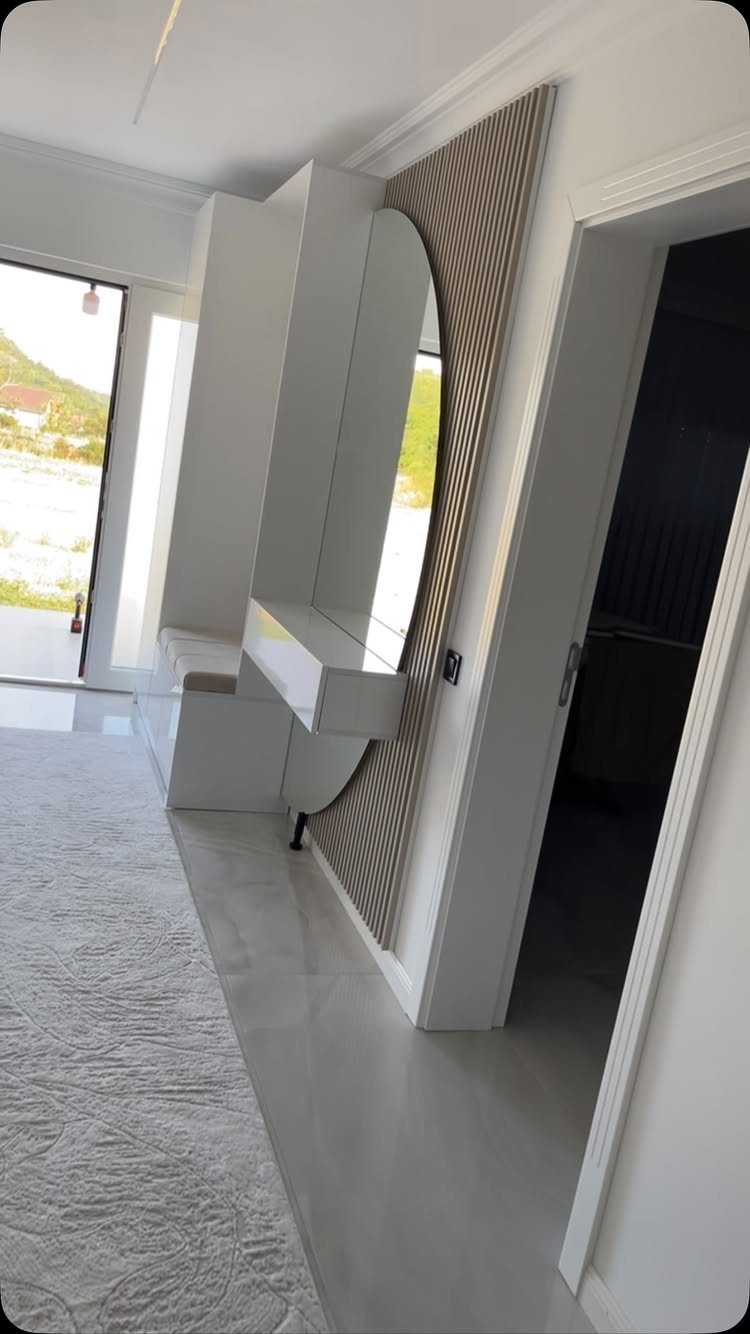 Modern white entryway with an arched mirror, built-in console, and grey runner rug.