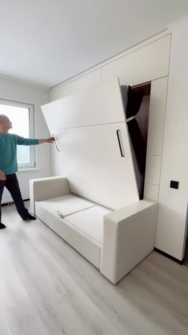 Man unfolding a white Murphy bed from a wall unit over a sofa.