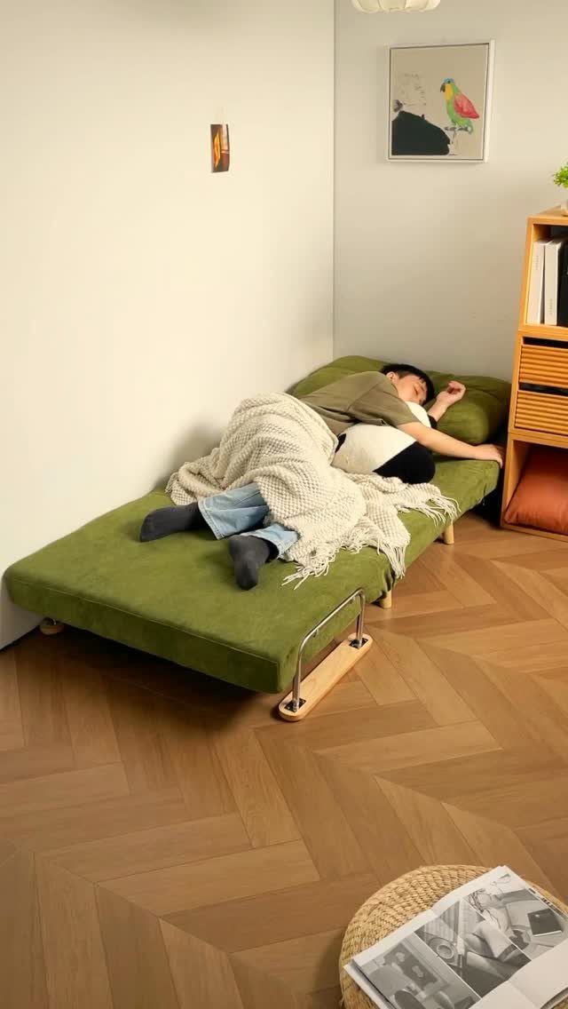 Person sleeping on a green multi-use sofa bed in a minimalist room