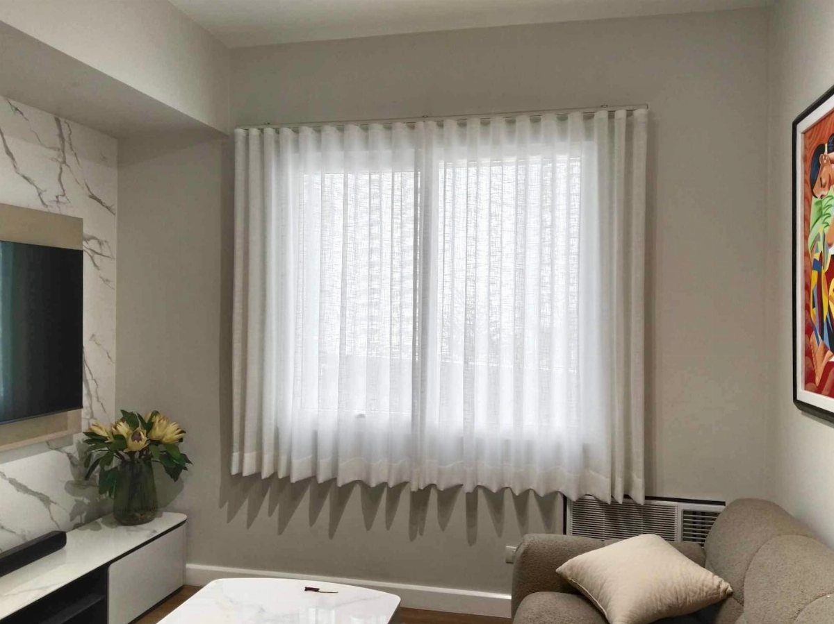 White sheer curtains hanging over a window in a bright, modern living room.