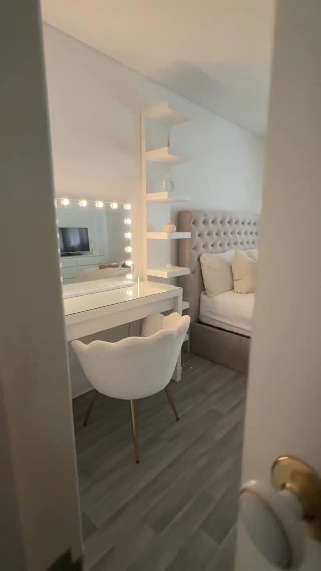 White vanity desk and modern chair next to a beige tufted bed.