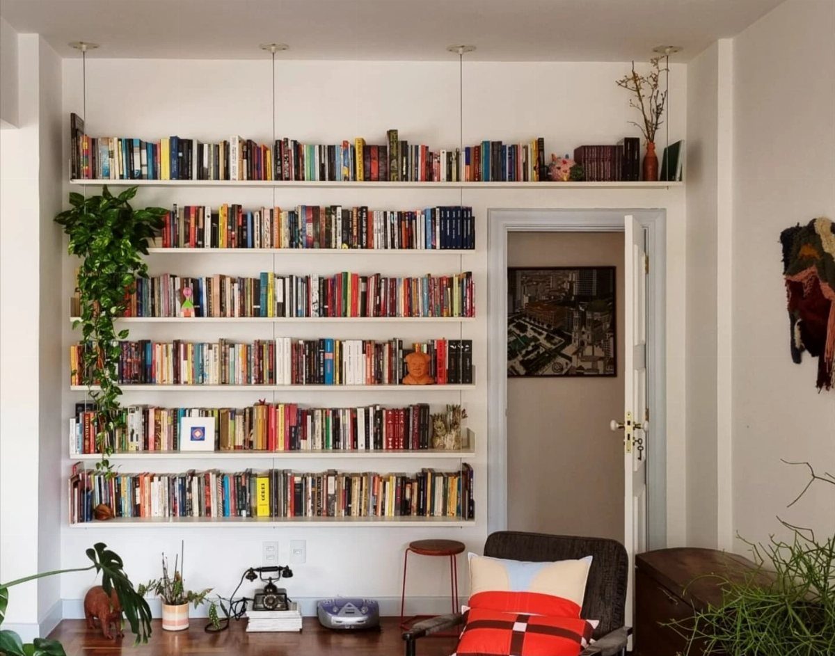 White floating bookshelves filled with colorful books and a trailing green plant.